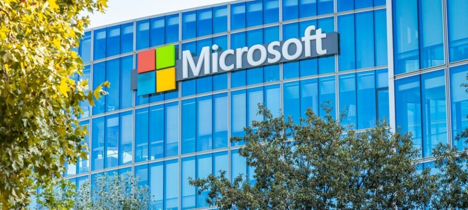 Microsoft logo on a blue glass office building partly obscured by trees