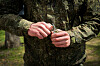 Camouflaged soldier holding a hand grenade with both hands outdoors.