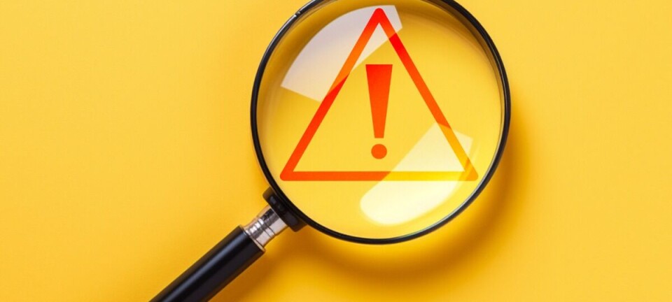 Magnifying glass over a red warning triangle with an exclamation mark on a yellow surface.