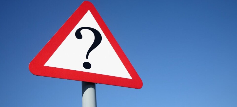 A triangular road sign with a question mark on a pole against a blue sky.